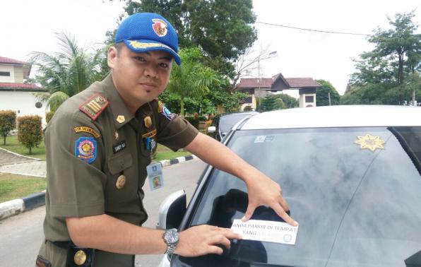 Kasi Operasi dan Pengendalian, Satpol PP Babel, Sandy Aji menempel stiker di kaca mobil yang parkir sembarangan.(foto: rell).